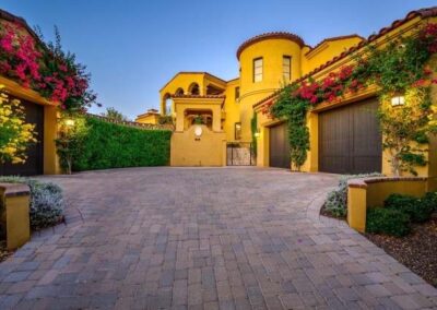 Custom curved paver driveway leading to a four-car garage and guest home, bordered by low retaining walls and flowering wall vines.